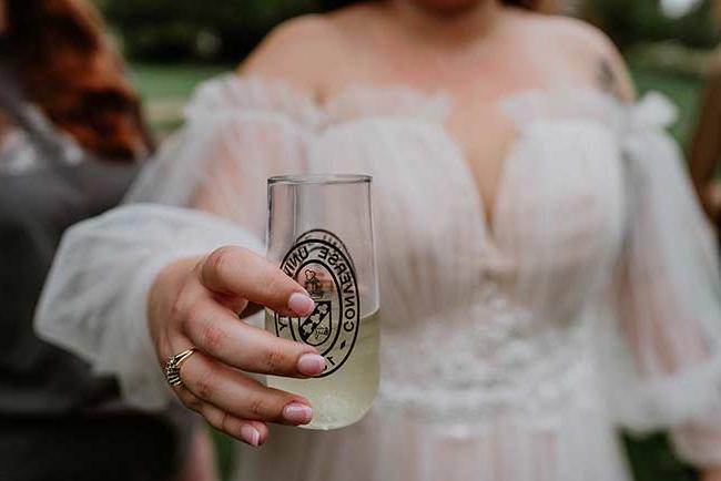 A bride holds a fancy glass with the Converse Unviersity logo on it